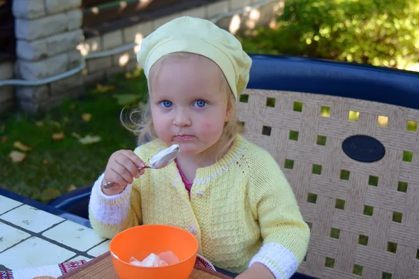 Girl sits in a chair and eats sour cream — Stock Photo, Image