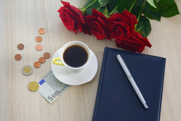 Taza blanca de café en la mesa, con rosas, bolígrafo y dinero — Foto de Stock