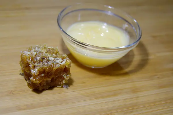 Crème de miel maison dans un bol et un morceau de cire d'abeille sur le woo — Photo