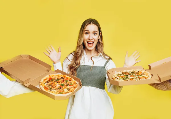 Emocional mujer joven sorprendida tratando de elegir pizza sobre fondo amarillo. Concepto de entrega de pizza. Imágenes De Stock Sin Royalties Gratis