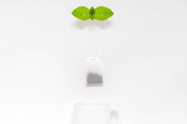 Düz bir yerde, beyaz kupanın üstünde taze nane şekeri olan çay poşeti. Çay molası kavramı