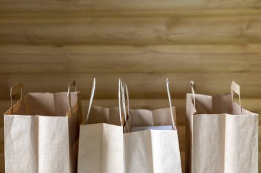 Ahşap arka planda saplı bir sürü kahverengi kağıt poşet var.