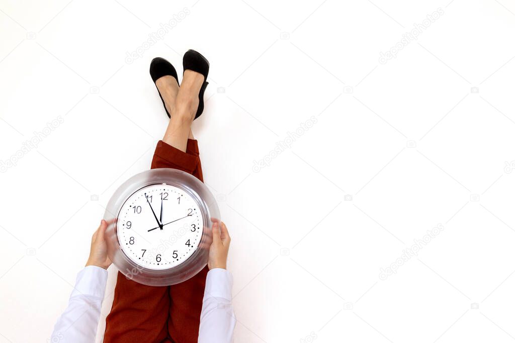 Legs in office suit and high heels up on the wall and holding office clock in hands with white background and copy space. Time management and job schedule concept.