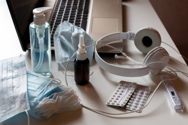 Yüz maskesi, dezenfektan, burun damlası, hap, kulaklık ve termometresi olan bir ev işi. Karantina için uzaktan çalışmaya hazırız. Laptoptaki karantina etiketi