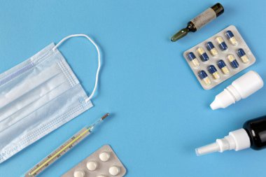 Virüsten tıbbi tedavi: yüz maskesi, haplar, damlalar, mavi arkaplanda termometre