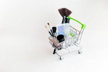 Makyaj malzemeleriyle alışveriş arabası: dekoratif gölgeler, fırçalar, ruj.