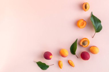 Pembe arka planda yeşil yapraklı, yarım dilimlenmiş, olgun kırmızı kayısılar ve çeyreklikler.