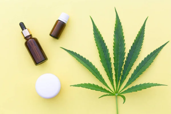Sarı zemin üzerinde kenevir yağı, kenevir yaprağı ve tohum bulunan şişe ve krema