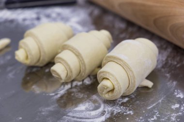 Un dolu bir masanın üzerindeki merdanenin yanında çiğ şeklinde kruvasanlar. El yapımı kruvasan hazırlık süreci.