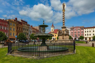 Broumov, Çek Cumhuriyeti - 17 Haziran 2020: Su çeşmesi, yeşil çimenler, renkli evler ve heykeli olan bir Marian sütunu ile kasaba meydanı manzarası. Mavi gökyüzü ve bulutlarla güneşli bir yaz günü.