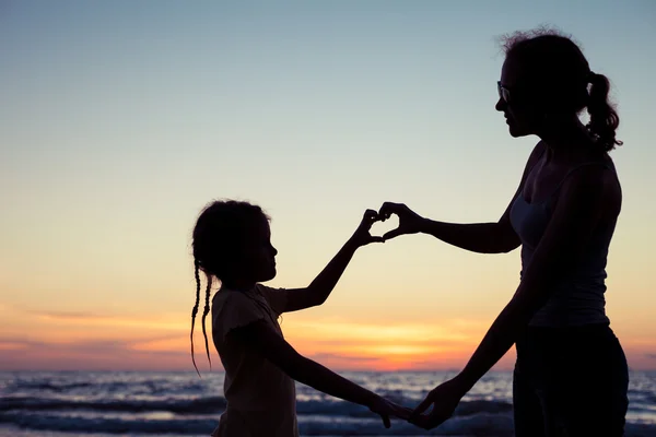 Mor och dotter spelar på stranden vid solnedgången tid. — Stockfoto