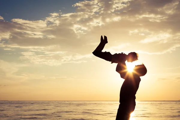 Far och son som spelar på stranden vid solnedgången tid. — Stockfoto