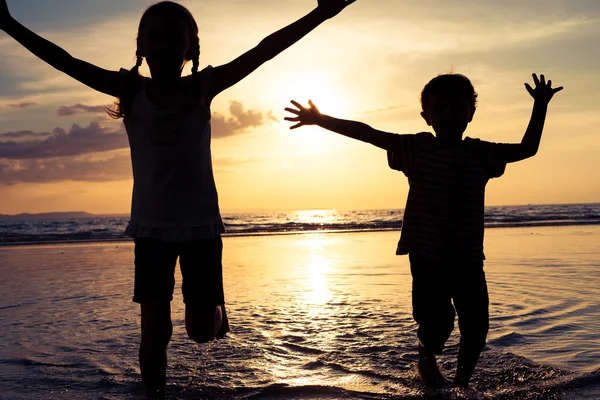 Crianças felizes brincando na praia na hora do pôr do sol . — Fotografia de Stock