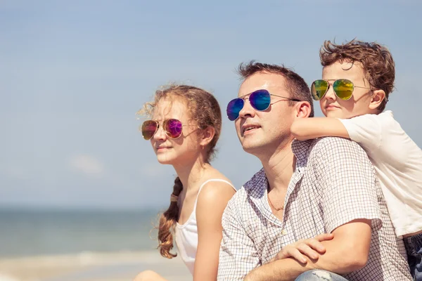 Pai e filhos sentados na praia durante o dia . — Fotografia de Stock