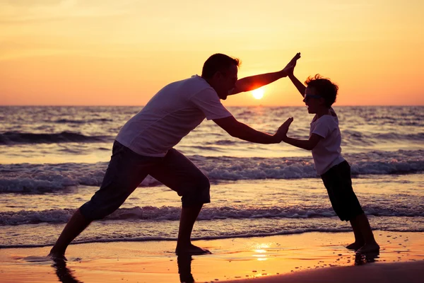 Pai e filho brincando na praia na hora do pôr do sol . — Fotografia de Stock