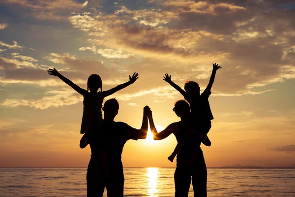 Silueta de familia feliz que juega en la playa al atardecer — Foto de Stock