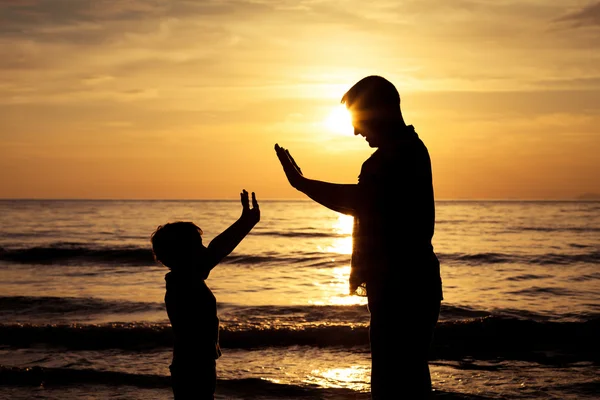 Vader en zoon spelen op het strand op de zonsondergang keer. — Stockfoto