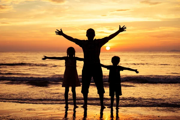 Pai e crianças brincando na praia na hora do pôr do sol . — Fotografia de Stock