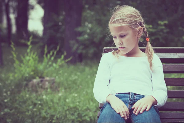 Portrait of sad blond little girl sitting on bench — Stock Photo, Image