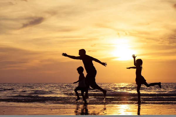 Far och barn som leker på stranden vid solnedgången tid. — Stockfoto