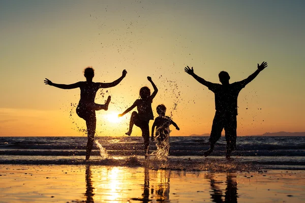 Silhueta de família feliz que de pé na praia nos sóis — Fotografia de Stock