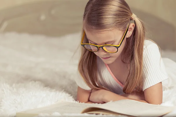Küçük kız yatakta yatıyordu ve kitap okuma — Stok fotoğraf