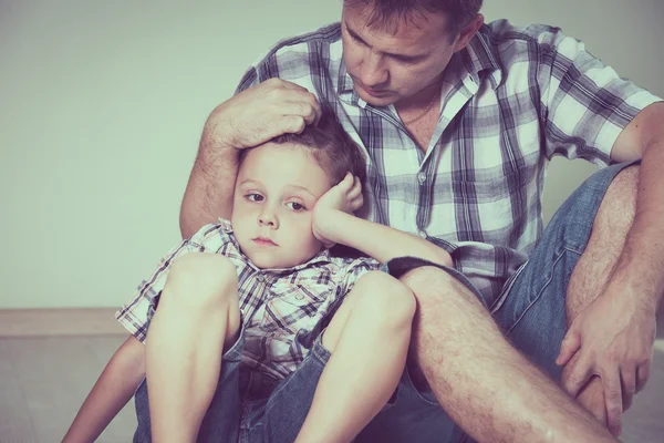 Triste filho e seu pai sentado no chão no quarto na hora do dia — Fotografia de Stock