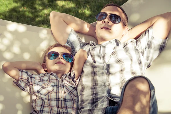 Far och son ligga i hängmatta i trädgården. — Stockfoto