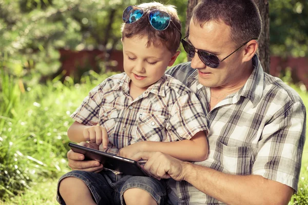 Vader en zoon zit in de buurt van de boom in de tuin. — Stockfoto