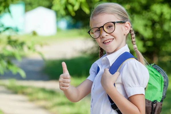 Criança de escola jovem sorridente em um uniforme escolar contra uma árvore em — Fotografia de Stock