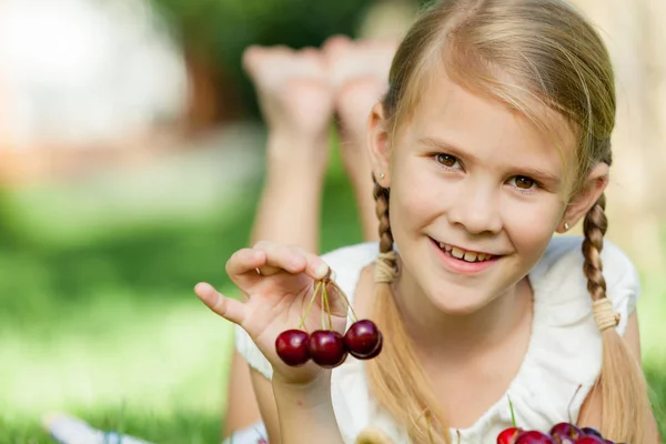 Happy little girl lying near the tree with a basket of cherries — Stock Photo, Image