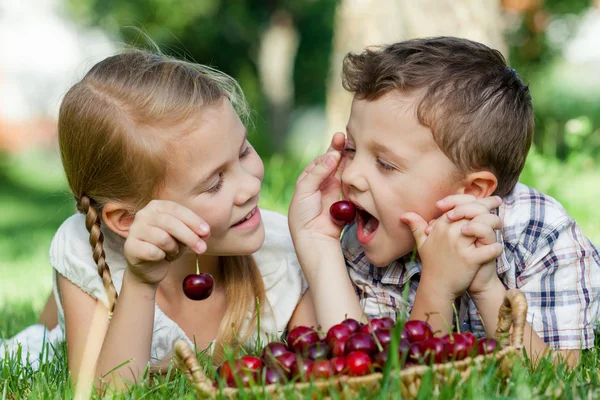 Gelukkig weinig kinderen liggen in de buurt van de boom met een mandje met cherr — Stockfoto