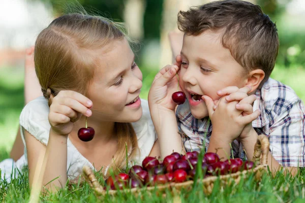 Happy little children lying near the tree with a basket of cherr — Stock Photo, Image