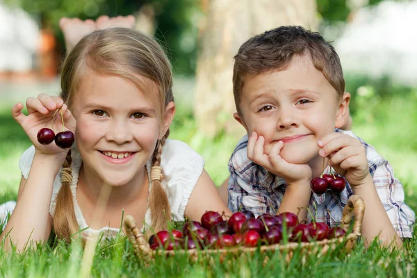 Happy little children lying near the tree with a basket of cherr — Stock Photo, Image