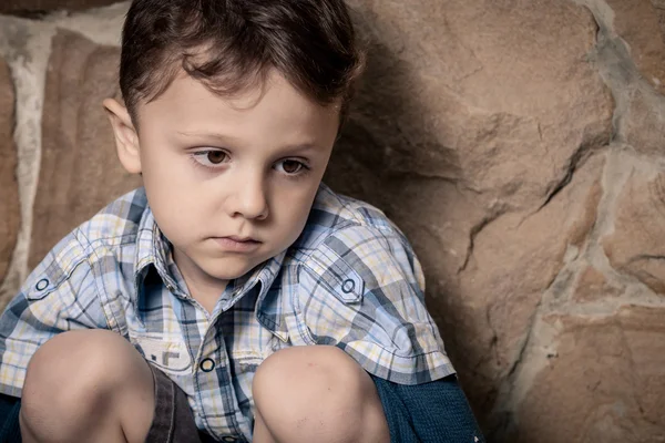 Грустный маленький мальчик сидит у стены — стоковое фото