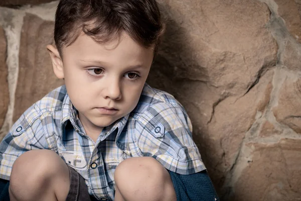 Pequeno menino triste sentado perto da parede — Fotografia de Stock