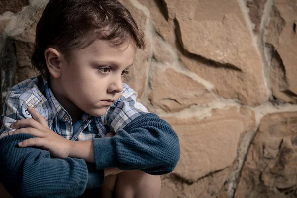 Ledsen liten pojke sitter nära väggen — Stockfoto