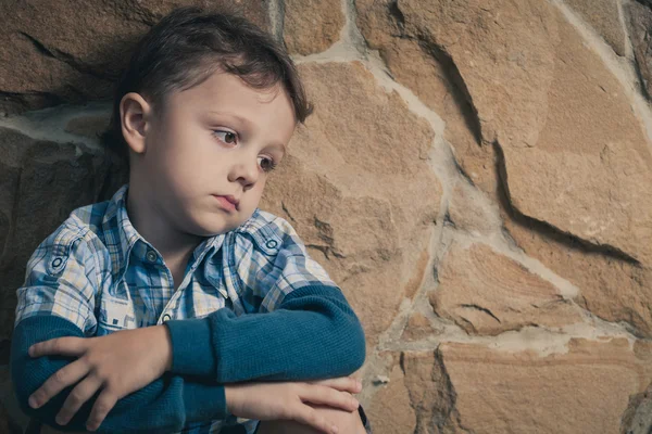 Niño triste sentado cerca de la pared —  Fotos de Stock
