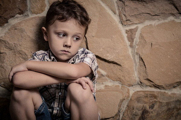 sad little boy sitting near the wall