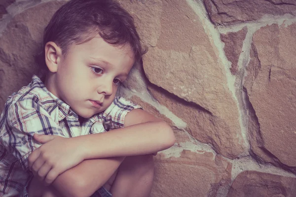 Triest kleine jongen zitten in de buurt van de muur — Stockfoto