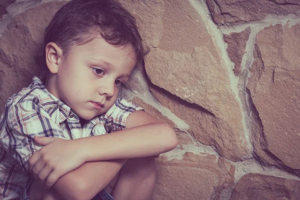 Niño triste sentado cerca de la pared — Foto de Stock