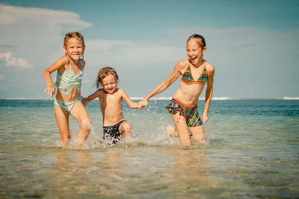 Tres niños felices jugando en la playa durante el día —  Fotos de Stock