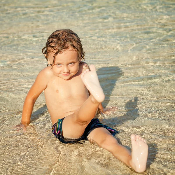 Kisfiú ül a strandon a nap idő — Stock Fotó