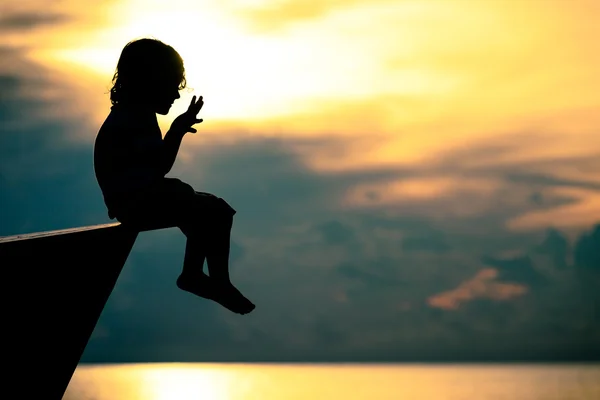 Glad liten pojke sitter på stranden i gryningen — Stockfoto