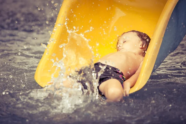 Little boy playing in the swimming pool on slide — Stock Photo, Image