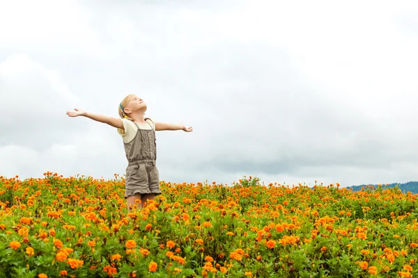 Gelukkig klein kind met verhoogde omhoog armen in groene gebied van bloemen. — Stockfoto