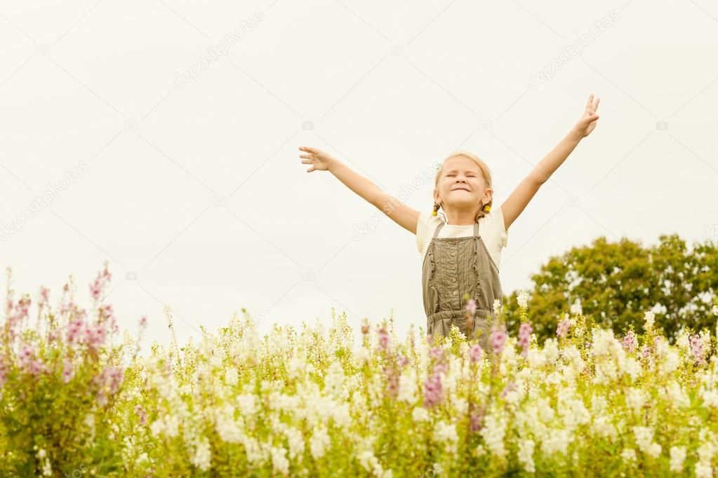 Happy little kid with raised up arms in green  field of flowers.