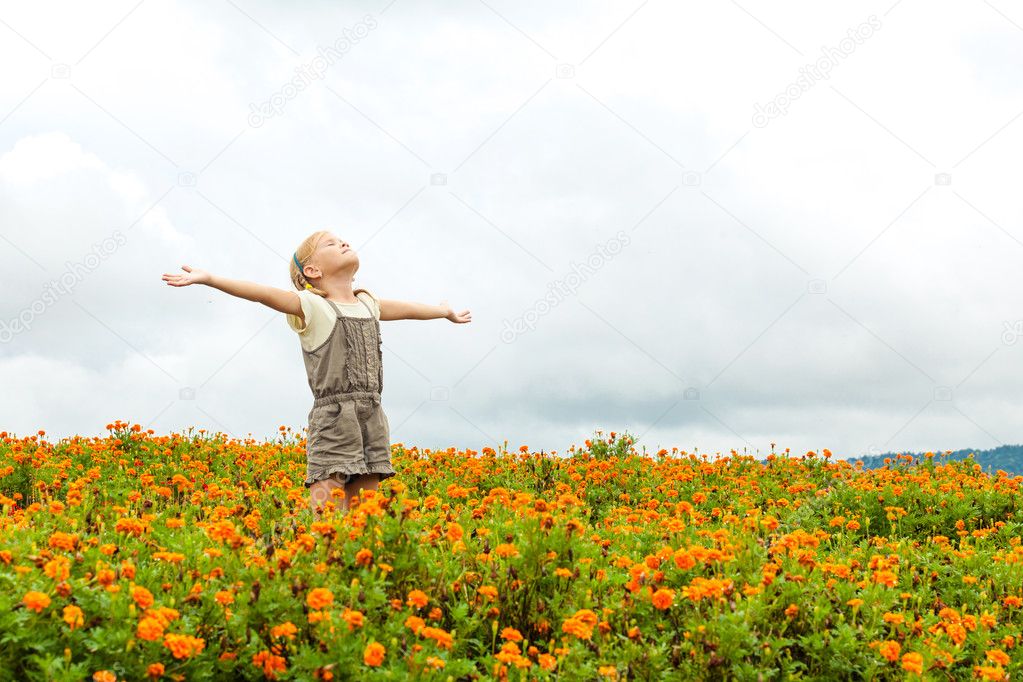 Happy little kid with raised up arms in green  field of flowers.