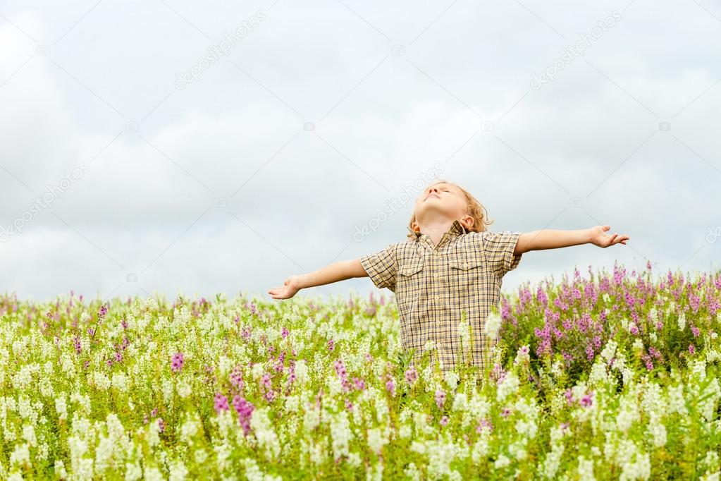 Happy little kid with raised up arms in green  field of flowers.