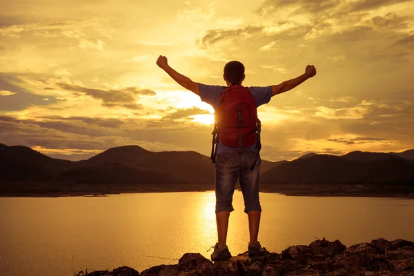 Uomo in piedi sulla riva di un lago di montagna e alza le braccia — Foto Stock